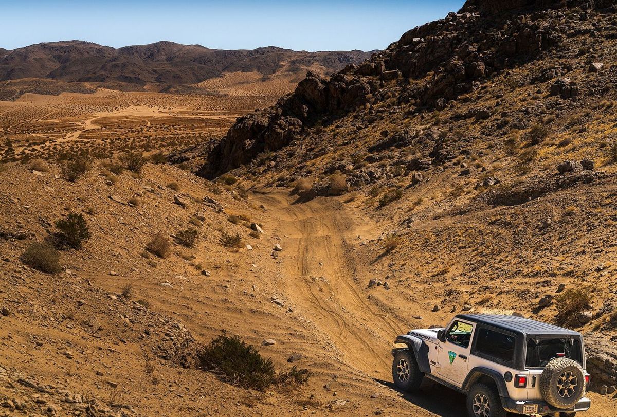 A Jeep climbing a sandy two-track through rocky Mojave Desert hills