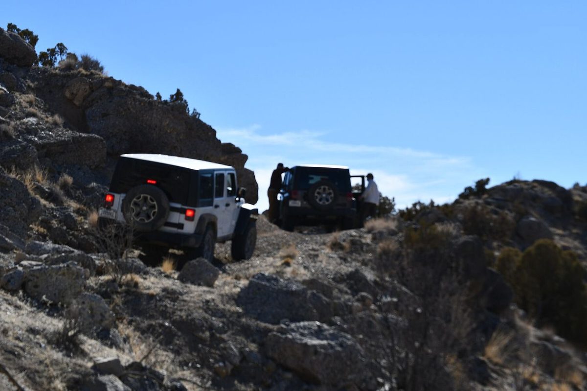 Two Jeeps climbing a rocky ledge trail under a blue Utah sky